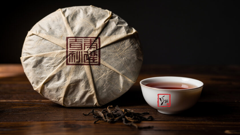 Bánh trà phổ nhĩ 357g gói giấy in mã số đặt trên bàn gỗ cùng chén trà