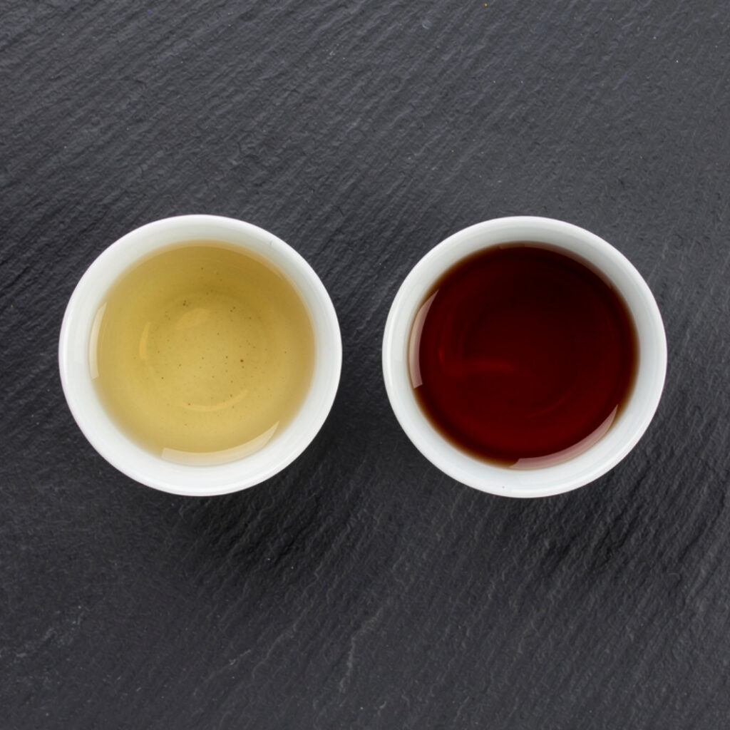 Hai chén phổ nhĩ đặt cạnh nhau, chén phổ nhĩ sống nước vàng xanh, chén phổ nhĩ chín nước đỏ nâu sẫm