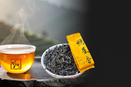 Phượng Hoàng Đơn Tùng Là Gì? Giải Mã "Hương Hình" Và Cái Tên "Áp Thỉ Hương" Chén trà phượng hoàng đơn tùng nước vàng óng bên lá trà xoăn dài, nền núi Phượng Hoàng mờ sương